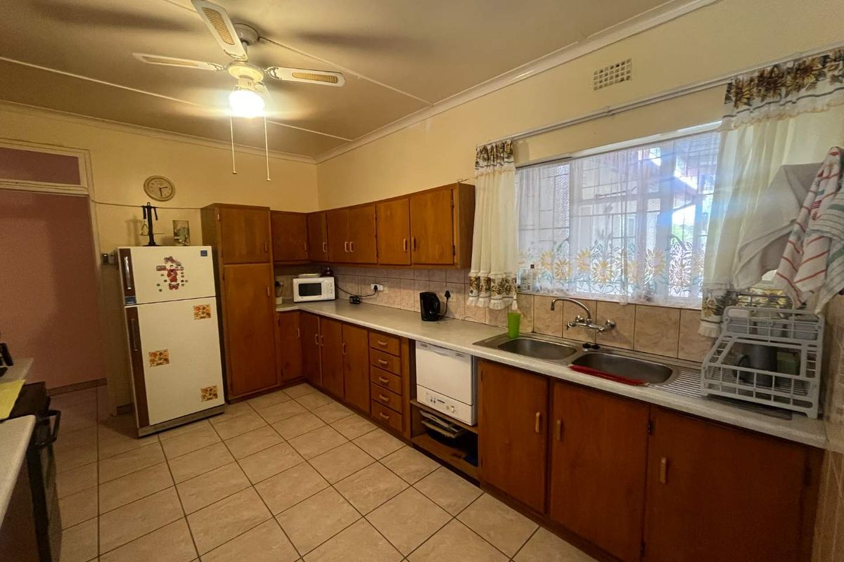 A functional kitchen featuring wooden cabinetry, tiled flooring, a double basin sink, and a ceiling fan, offering a classic layout with potential for modernization.