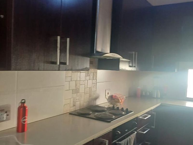 A functional kitchen featuring dark wood cabinetry, a stone tile backsplash, and integrated appliances including an electric hob and oven.