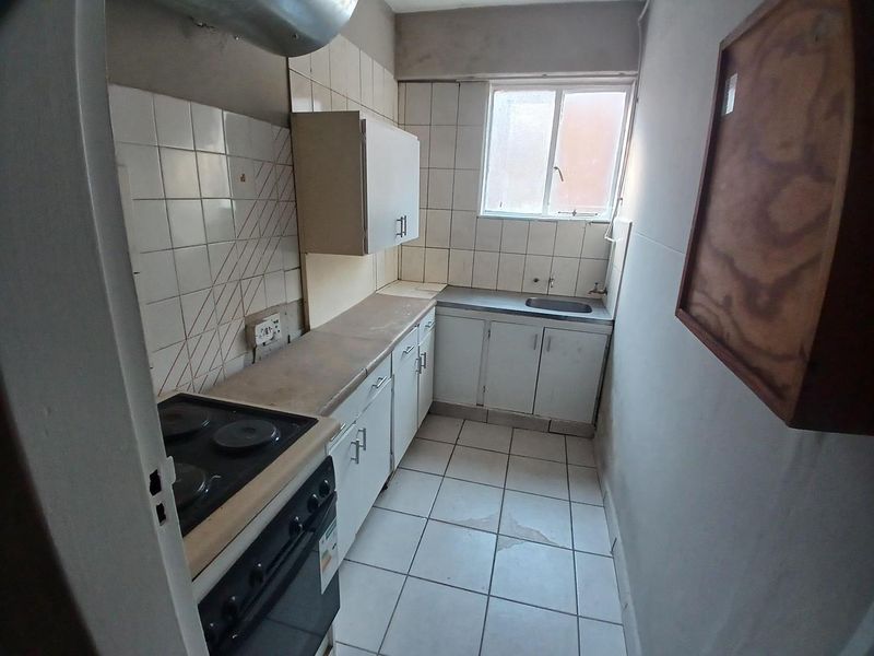 A compact, dated kitchen featuring built-in cabinetry, a stainless steel sink, and an electric stove, requiring cosmetic updates to modernize the space.