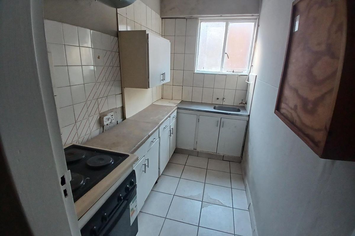 A compact, dated kitchen featuring built-in cabinetry, a stainless steel sink, and an electric stove, requiring cosmetic updates to modernize the space.