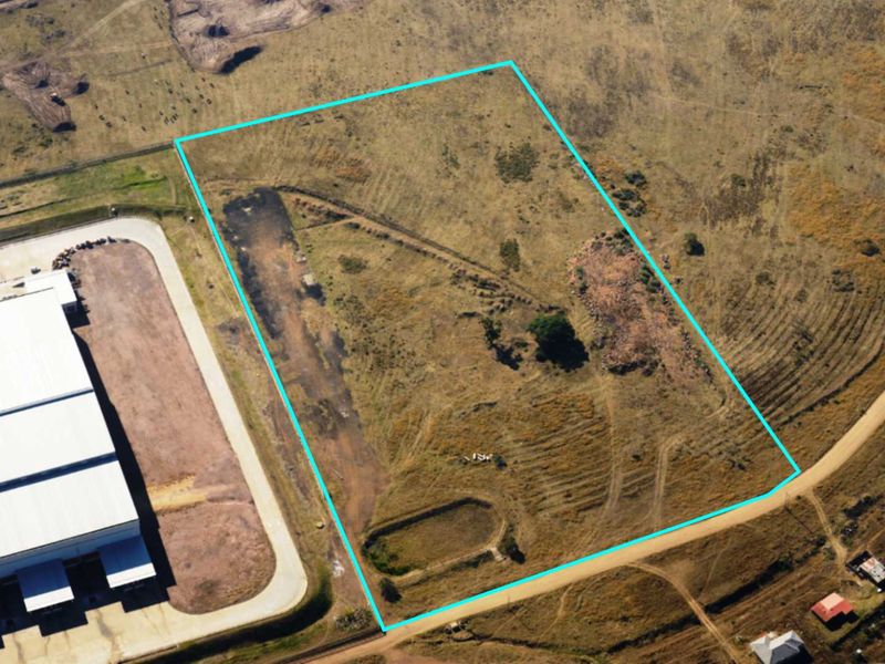 Aerial view of a vacant commercial land plot with defined boundaries, featuring natural terrain and adjacent access roads.