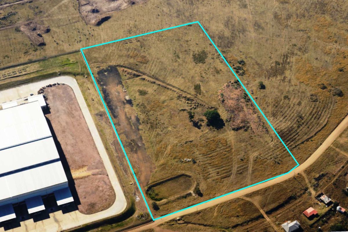 Aerial view of a vacant commercial land plot with defined boundaries, featuring natural terrain and adjacent access roads.
