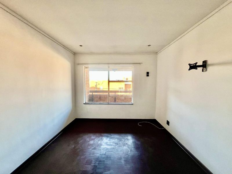 An empty bedroom featuring dark flooring, recessed downlights, and a wall-mounted TV bracket, offering a blank canvas for personalization.
