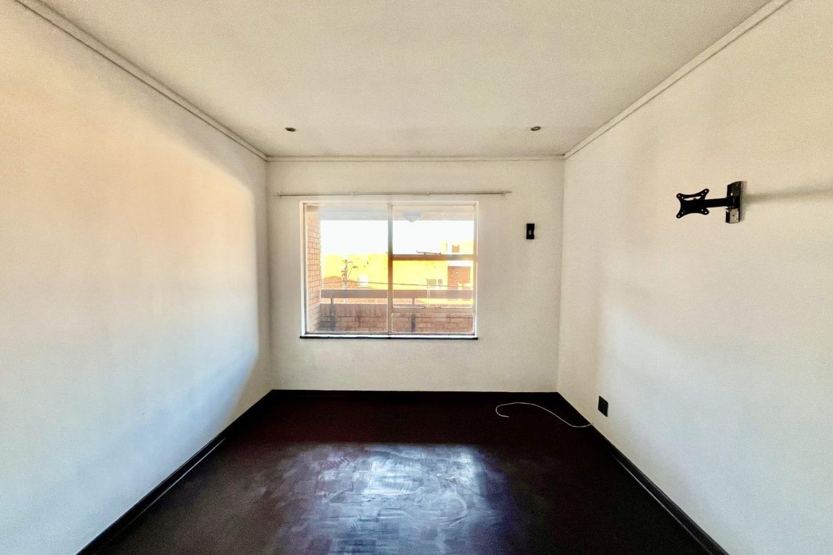 An empty bedroom featuring dark flooring, recessed downlights, and a wall-mounted TV bracket, offering a blank canvas for personalization.