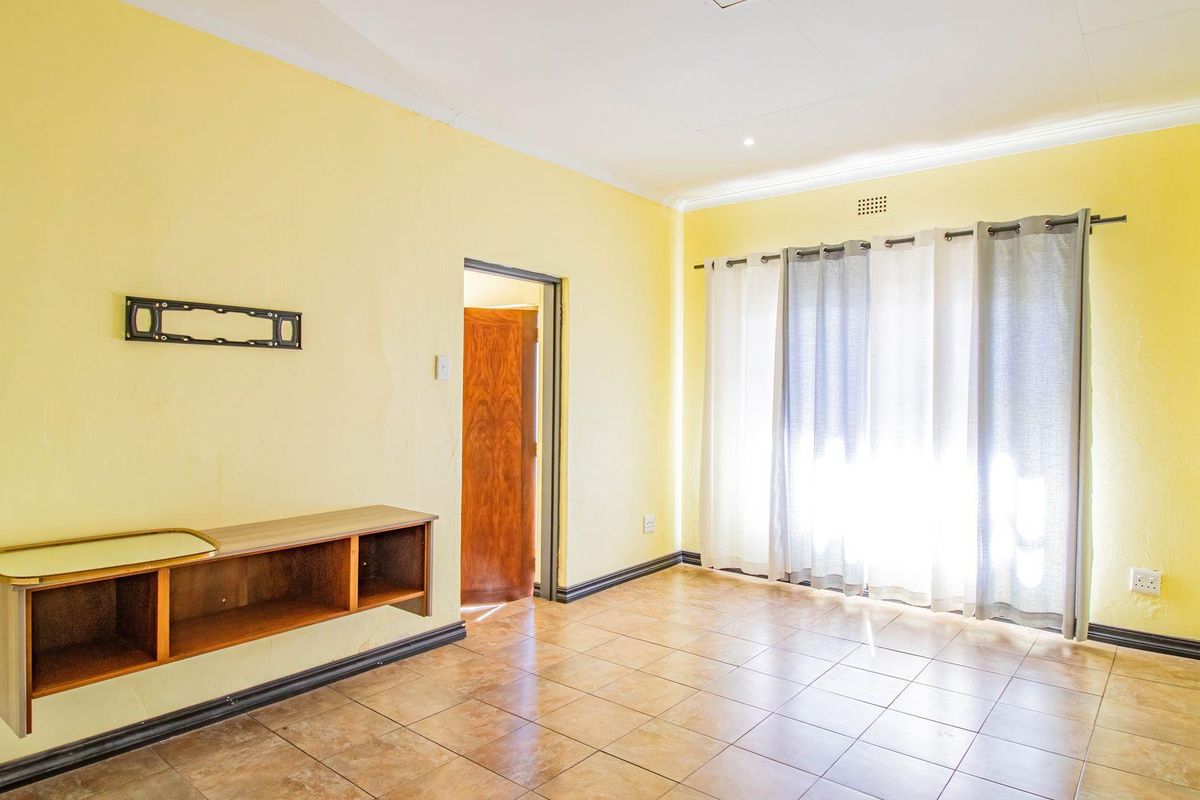 A bright living room featuring tiled flooring, a built-in wall-mounted shelf, and large windows with curtains.