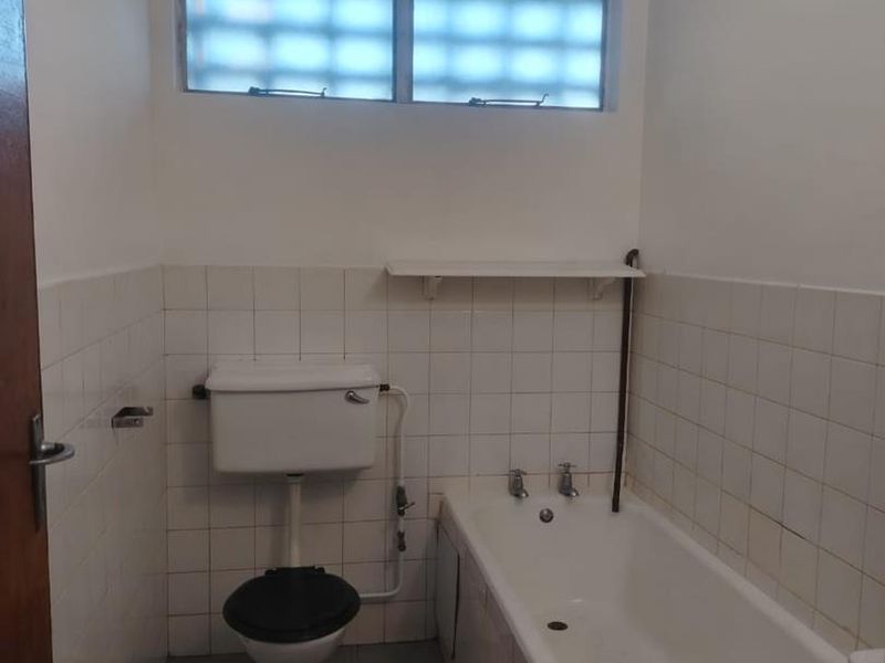 A dated bathroom featuring a standard bathtub, toilet, and tiled finishes, requiring cosmetic updates to modernize the space.