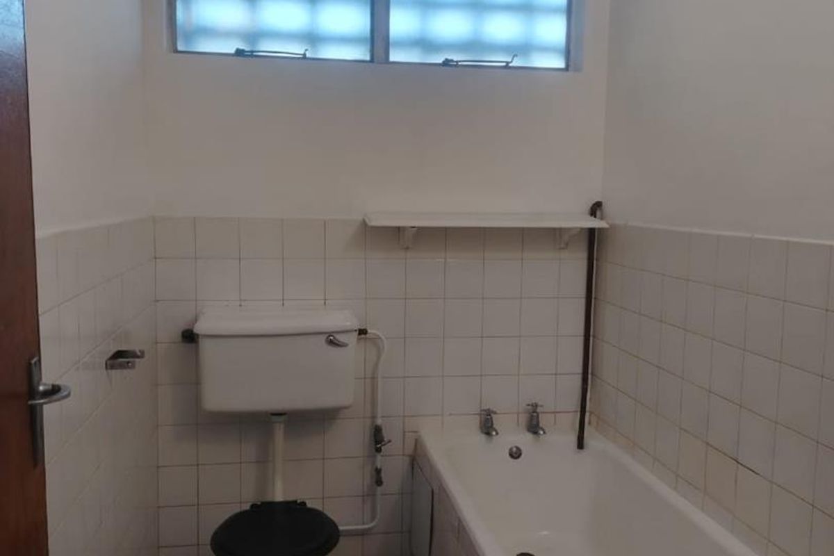 A dated bathroom featuring a standard bathtub, toilet, and tiled finishes, requiring cosmetic updates to modernize the space.
