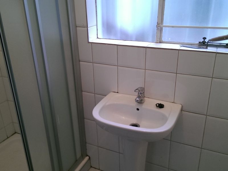 A compact bathroom featuring a pedestal basin, shower enclosure, and white wall tiling, requiring cosmetic updates to improve its overall condition.
