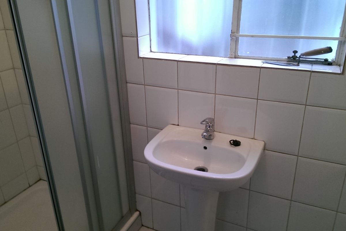 A compact bathroom featuring a pedestal basin, shower enclosure, and white wall tiling, requiring cosmetic updates to improve its overall condition.