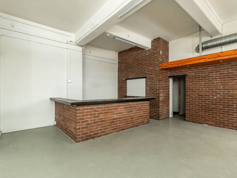 An empty bar area featuring exposed brick walls, a built-in brick counter, and industrial-style exposed ceiling beams and ventilation ducting.