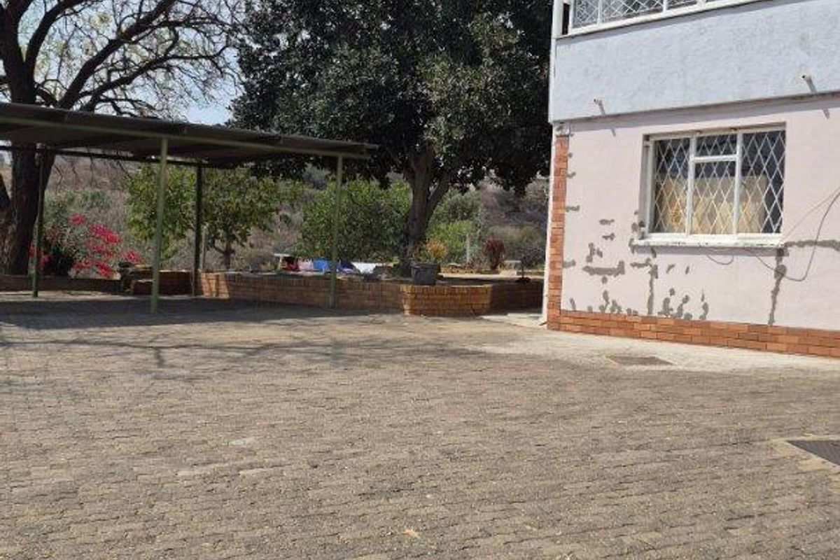 Rear exterior view featuring a paved driveway, a metal carport structure, and a multi-story building with visible exterior wall finish deterioration.