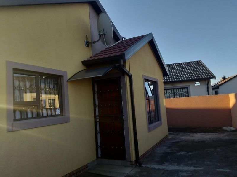 Front exterior view of a residential house featuring a tiled roof, security gate, and window burglar bars with a paved driveway area.