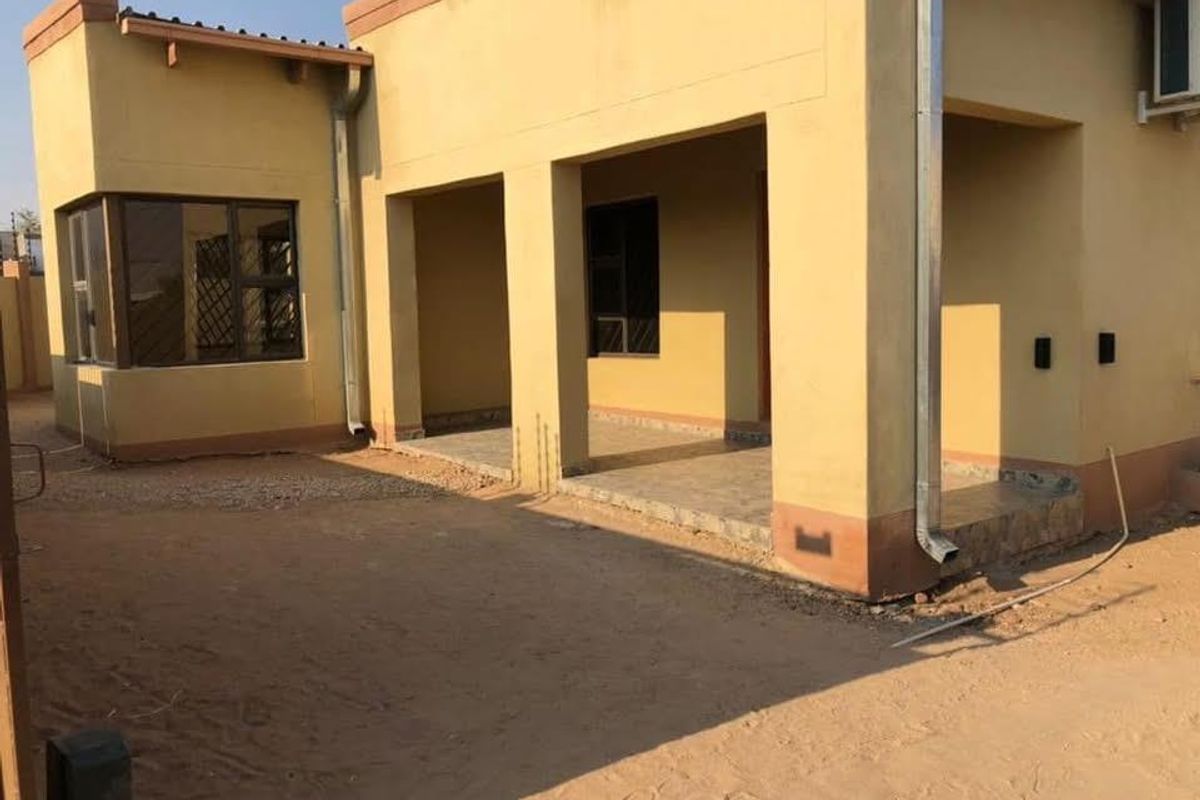 Rear view of the property featuring a covered patio area with tiled flooring and exterior downpipes, set against an unfinished garden space.