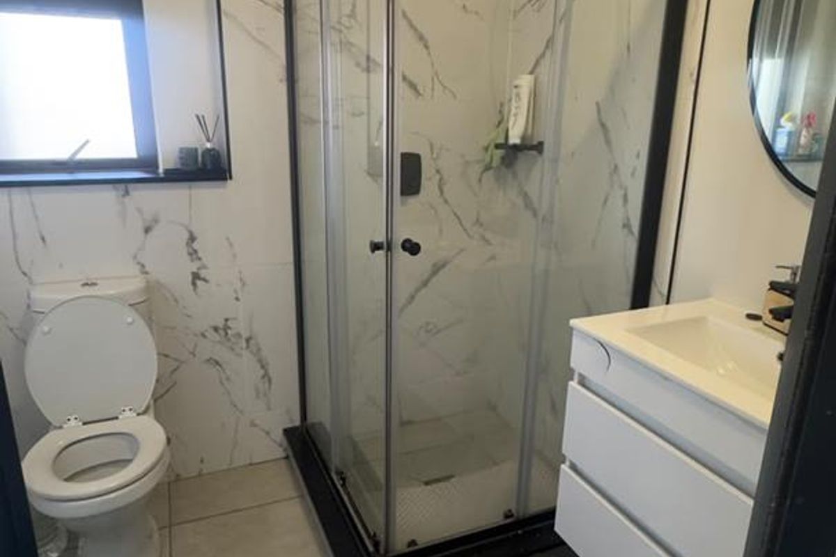 A modern bathroom featuring a glass shower enclosure, vanity cabinet with basin, and marble-look wall tiling. Note visible ceiling water staining.