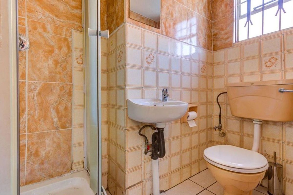A compact bathroom featuring a shower enclosure, wall-mounted basin, and toilet, finished with dated ceramic wall and floor tiles.