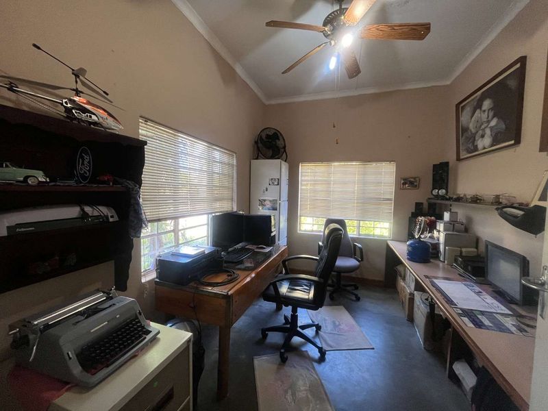 A functional home office space featuring built-in desk surfaces, shelving, ceiling fan, and dual windows with venetian blinds.