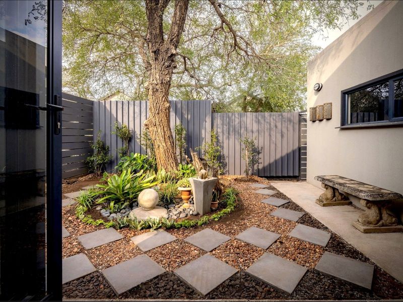 A well-maintained rear courtyard featuring a mature tree, gravel landscaping, paved stepping stones, and modern timber slat fencing.