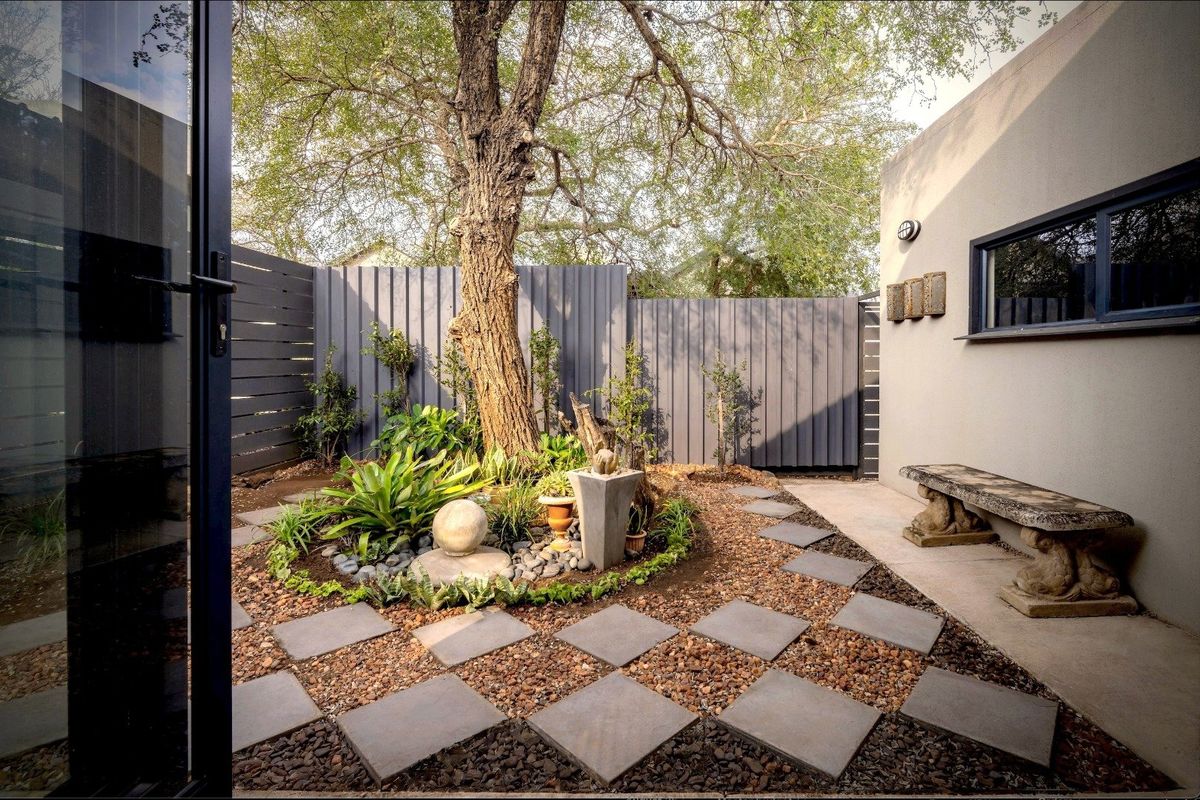 A well-maintained rear courtyard featuring a mature tree, gravel landscaping, paved stepping stones, and modern timber slat fencing.