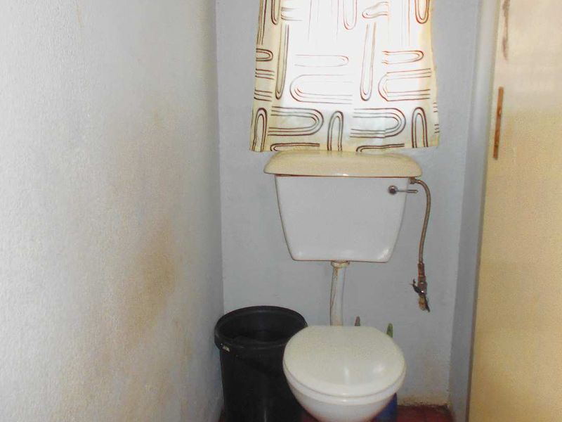 A small, dated bathroom featuring a standard toilet and tiled flooring, currently showing signs of wear and wall staining.