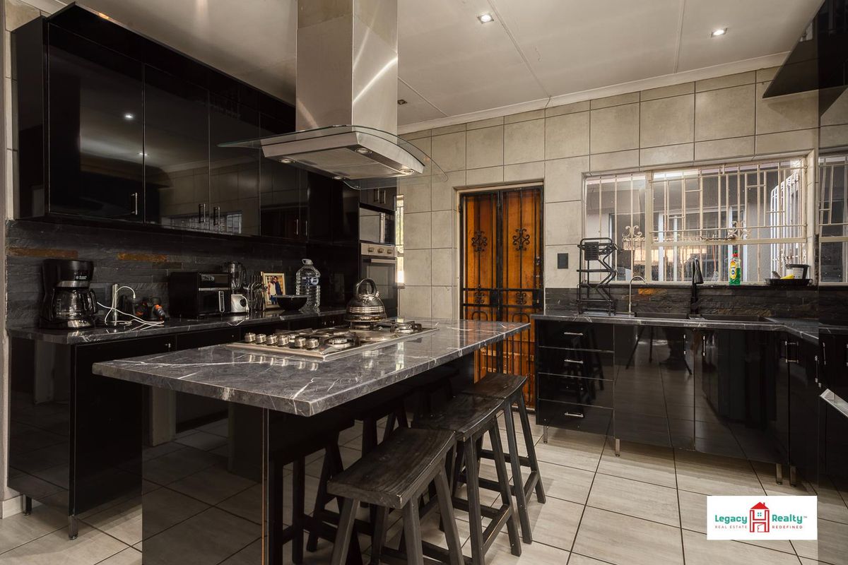 Modern kitchen featuring high-gloss black cabinetry, stone countertops, a central island with a built-in gas hob, and a stainless steel extractor fan.