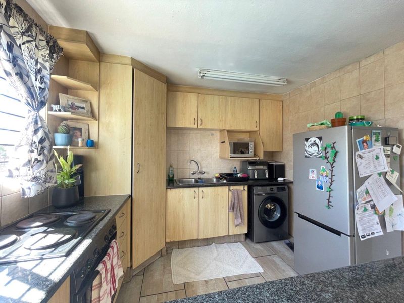 A functional kitchen featuring built-in wooden cabinetry, a tiled backsplash, a hob, an oven, and tiled flooring with space for integrated appliances.