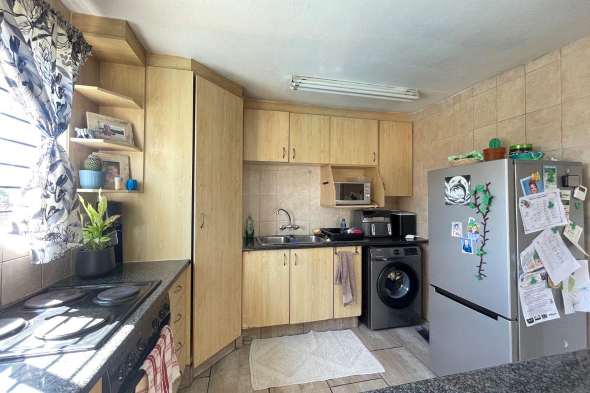 A functional kitchen featuring built-in wooden cabinetry, a tiled backsplash, a hob, an oven, and tiled flooring with space for integrated appliances.