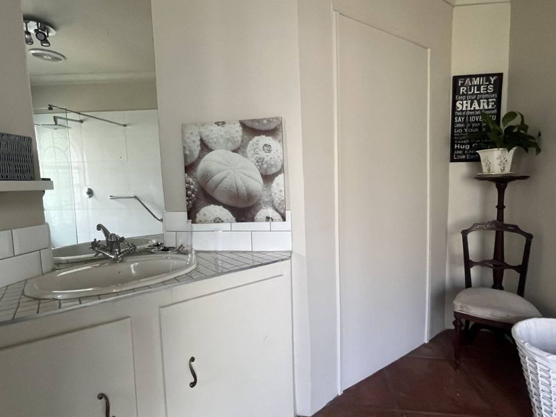 A functional bathroom featuring a vanity with a tiled countertop, inset sink, and a glass-enclosed shower area.