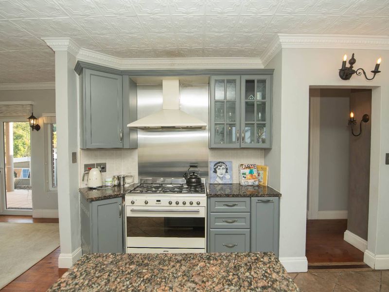 A well-appointed kitchen featuring grey cabinetry, granite countertops, a stainless steel splashback, and a built-in gas stove with an extractor fan.