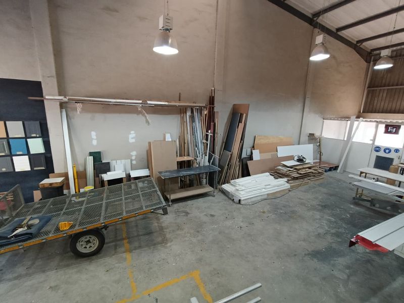 Spacious industrial utility area featuring high ceilings, exposed steel roof structure, concrete flooring, and industrial pendant lighting, suitable for workshop or storage use.