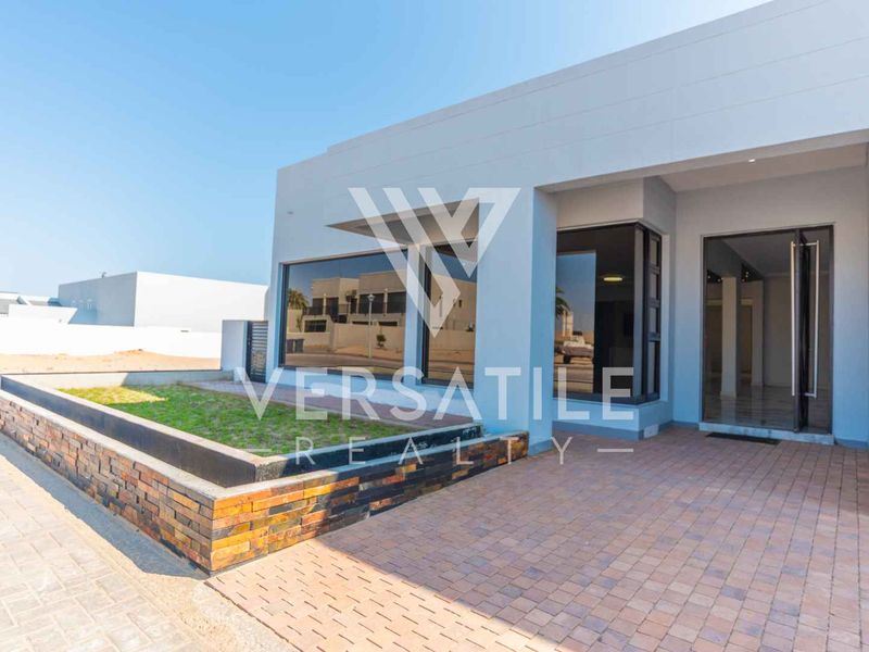 Modern front facade featuring a paved entrance, raised garden bed with stone cladding, and large glass windows providing a clean, contemporary aesthetic.