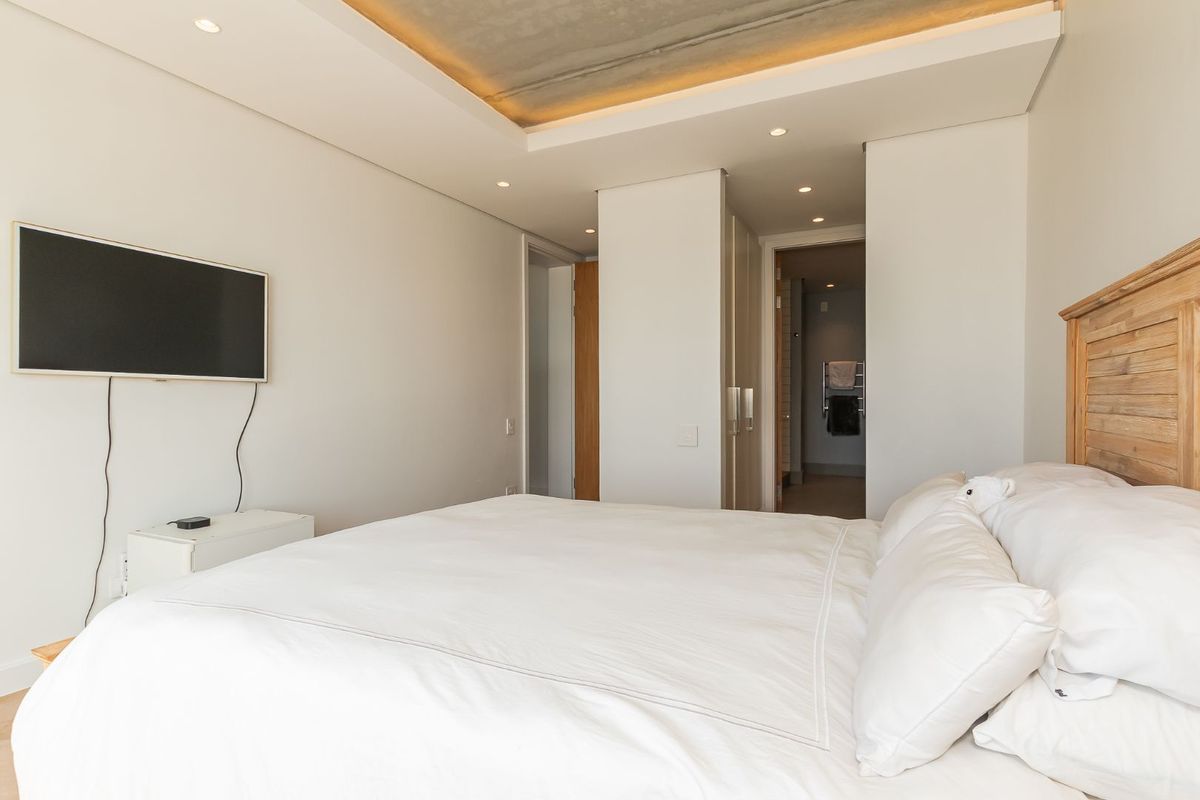 Modern bedroom featuring a recessed ceiling with ambient lighting, built-in cabinetry, and an en-suite bathroom access.