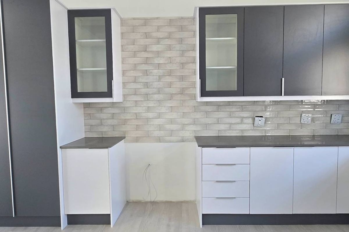 Modern kitchen featuring two-tone cabinetry, stone-look countertops, and a decorative brick-style tiled backsplash, currently awaiting final appliance installation.