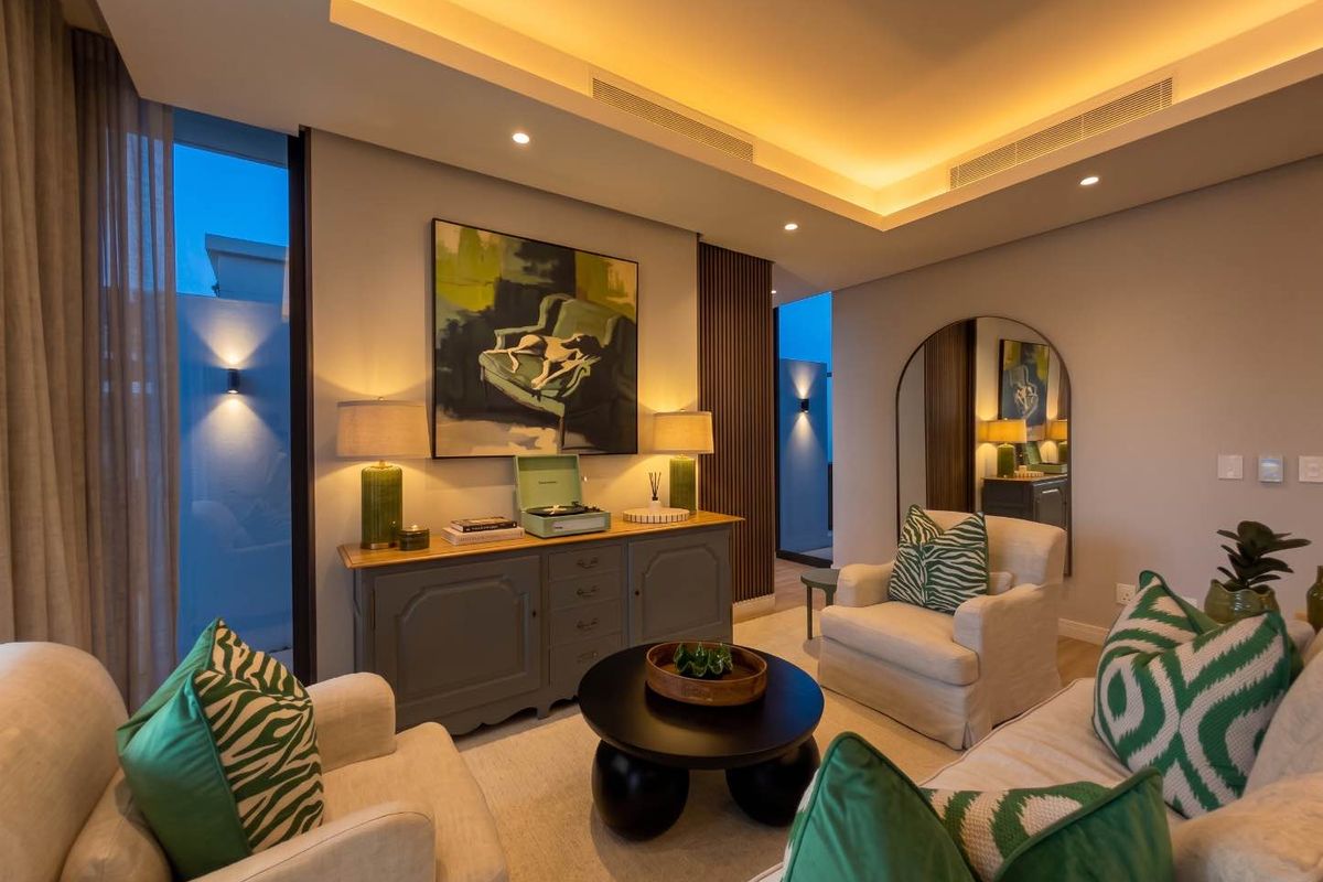 A modern, well-lit living room featuring a recessed ceiling with cove lighting, ducted air conditioning, and elegant timber wall paneling.