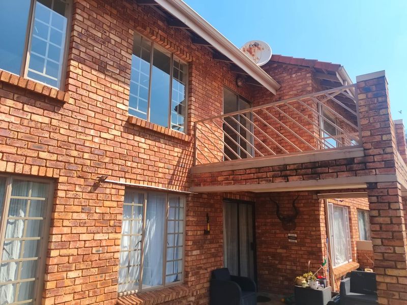 Rear view of a double-story townhouse featuring a face brick facade, a balcony with a metal balustrade, and sliding door access.