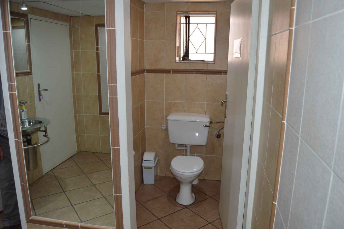 A compact bathroom featuring tiled walls and flooring, a standard toilet, and a wall-mounted basin with a large mirror.