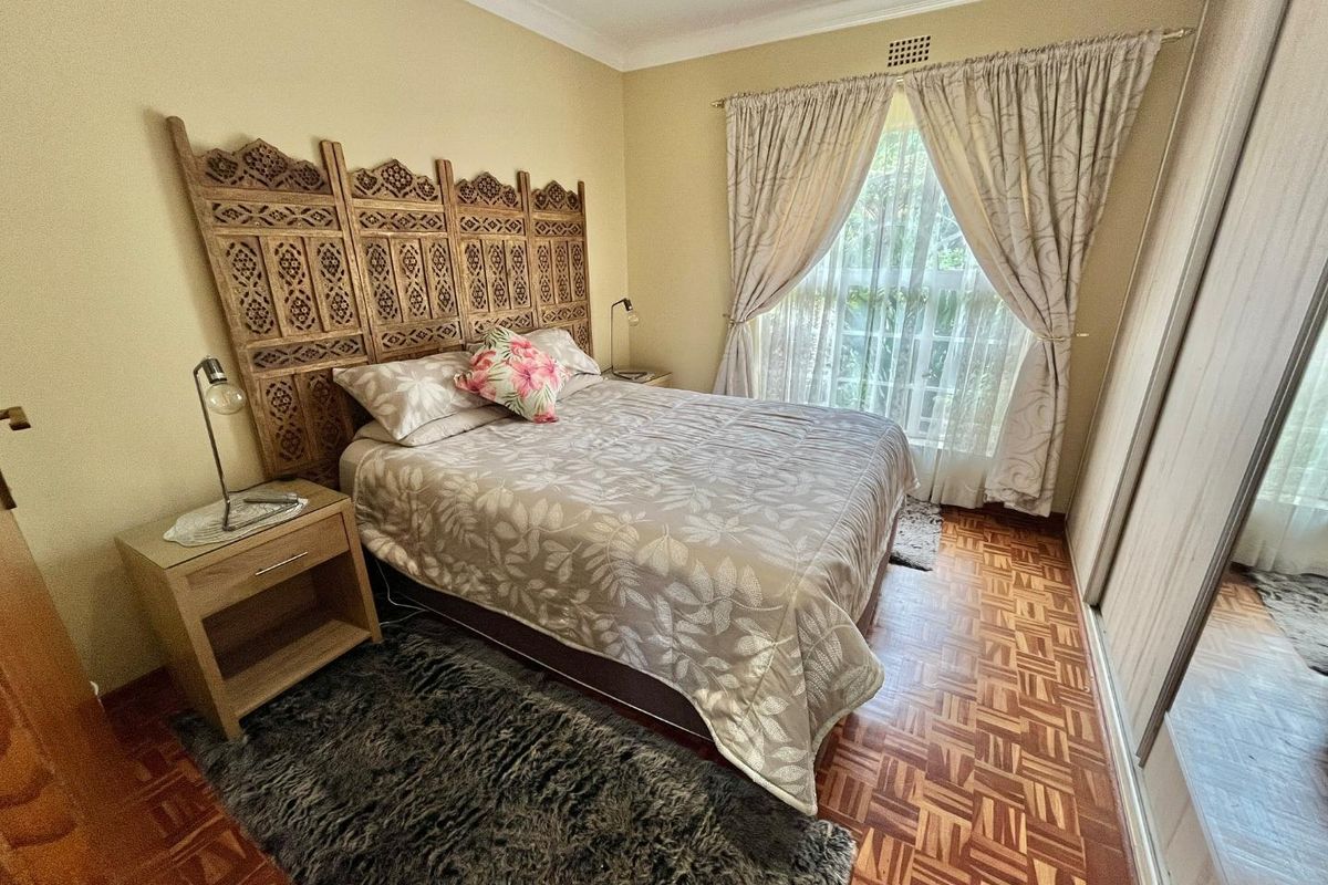 A bedroom featuring parquet flooring, built-in sliding door cupboards, and a window with curtaining.