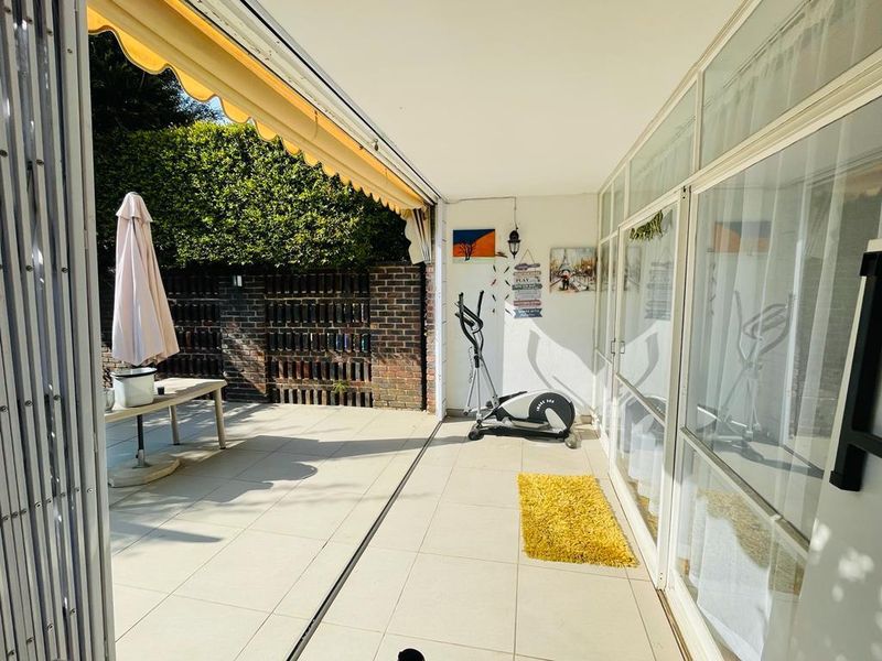 A spacious covered patio featuring tiled flooring, a retractable awning, and large sliding glass doors, providing a seamless transition to the outdoor area.