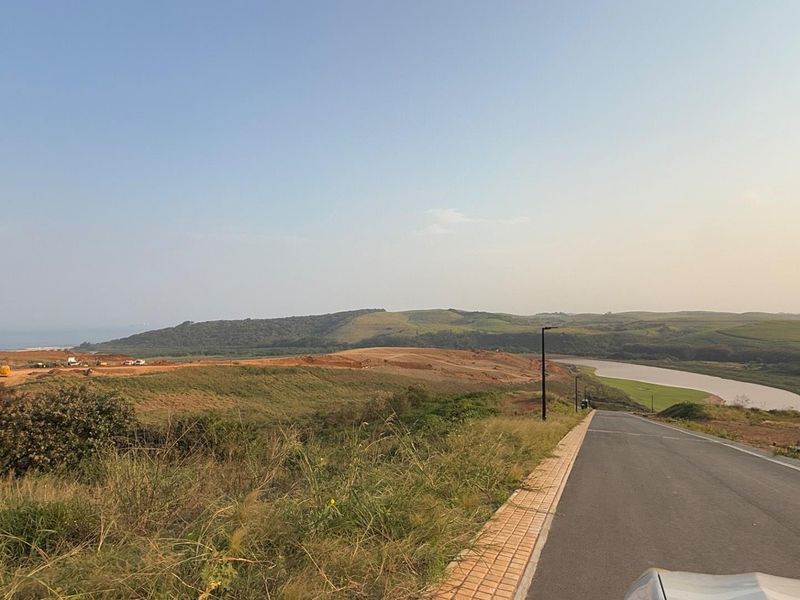 A view of a paved residential street leading through a developing landscape with rolling hills and a nearby river.