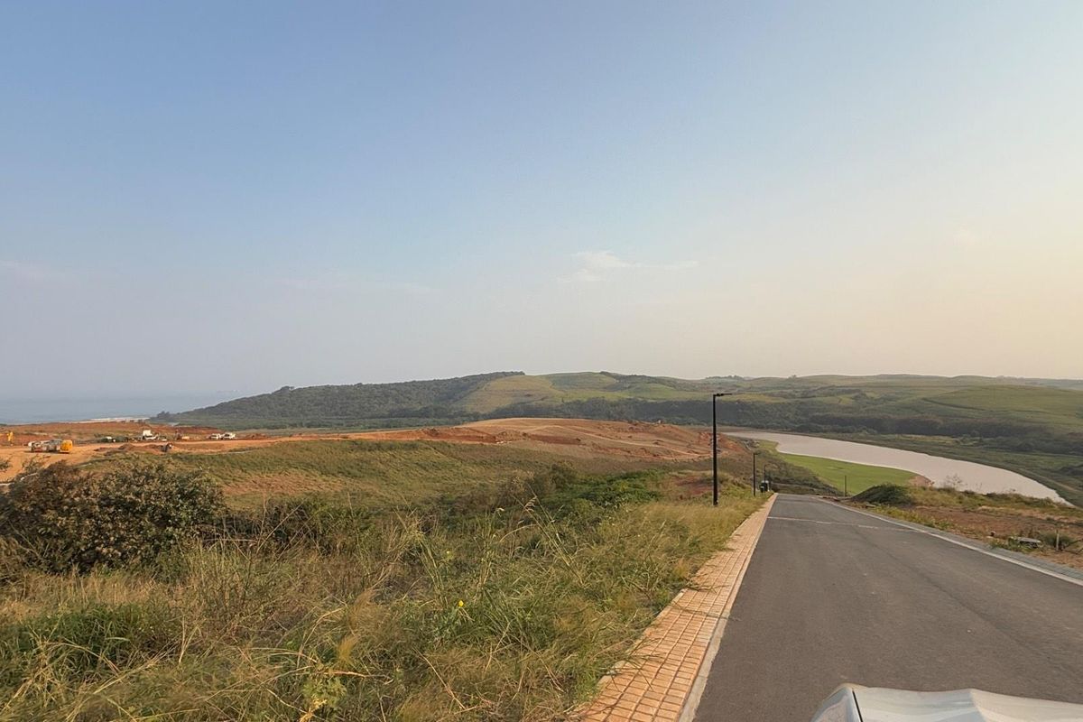 A view of a paved residential street leading through a developing landscape with rolling hills and a nearby river.