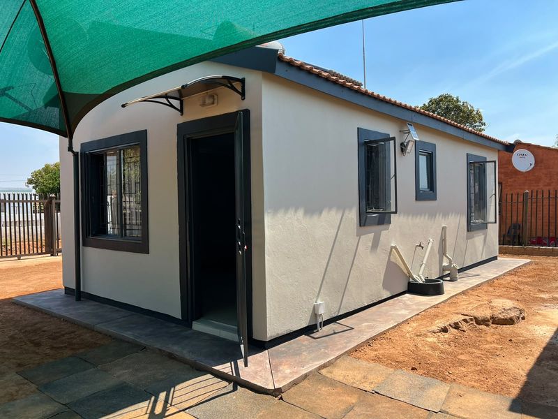 Rear view of a detached structure featuring a tiled patio, security bars on windows, and an installed shade sail.