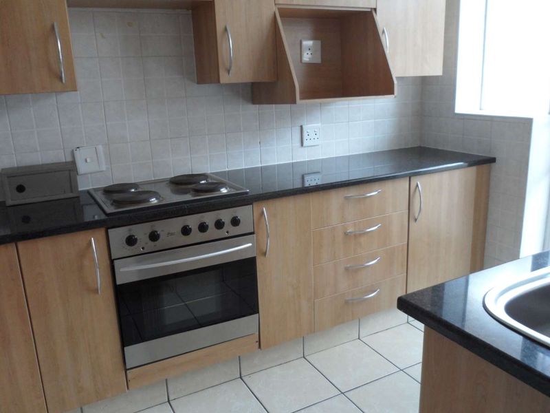 A functional kitchen featuring light wood cabinetry, dark granite countertops, a built-in electric oven and hob, and tiled flooring.