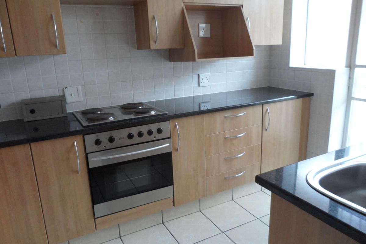 A functional kitchen featuring light wood cabinetry, dark granite countertops, a built-in electric oven and hob, and tiled flooring.