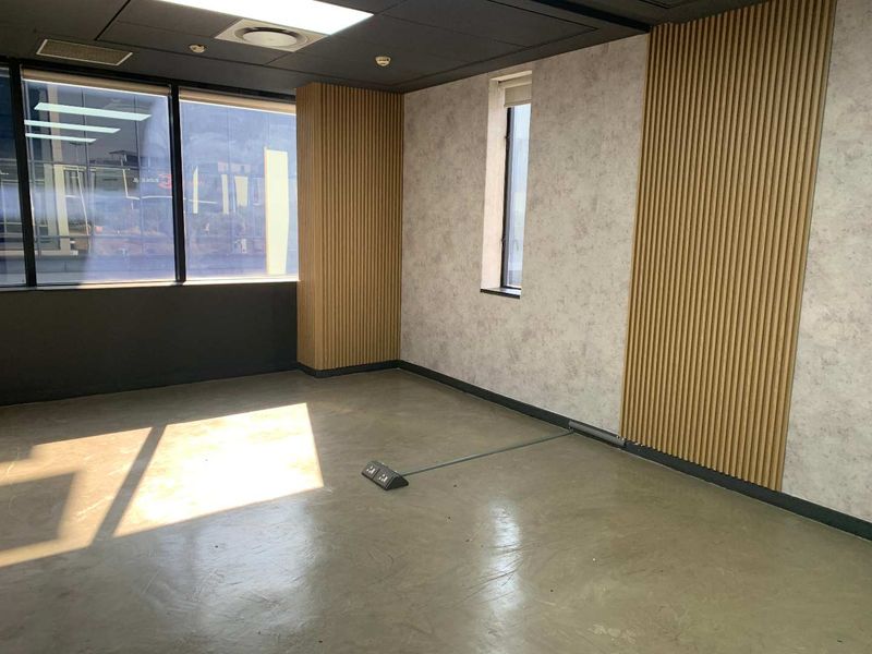 Modern empty office space featuring polished concrete floors, timber slat wall accents, large windows, and integrated floor power connectivity.