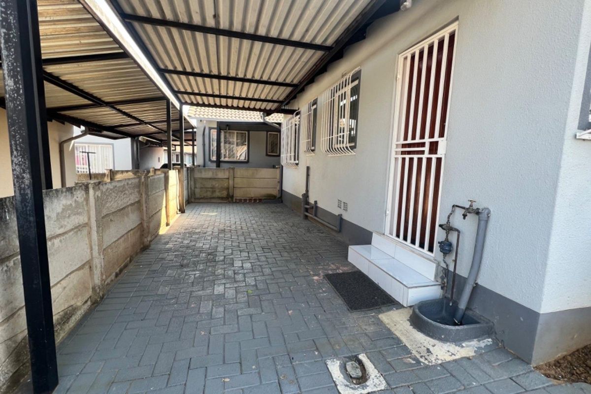 A paved rear exterior area featuring a covered carport, secure gated access, and functional utility fixtures including an external water tap.