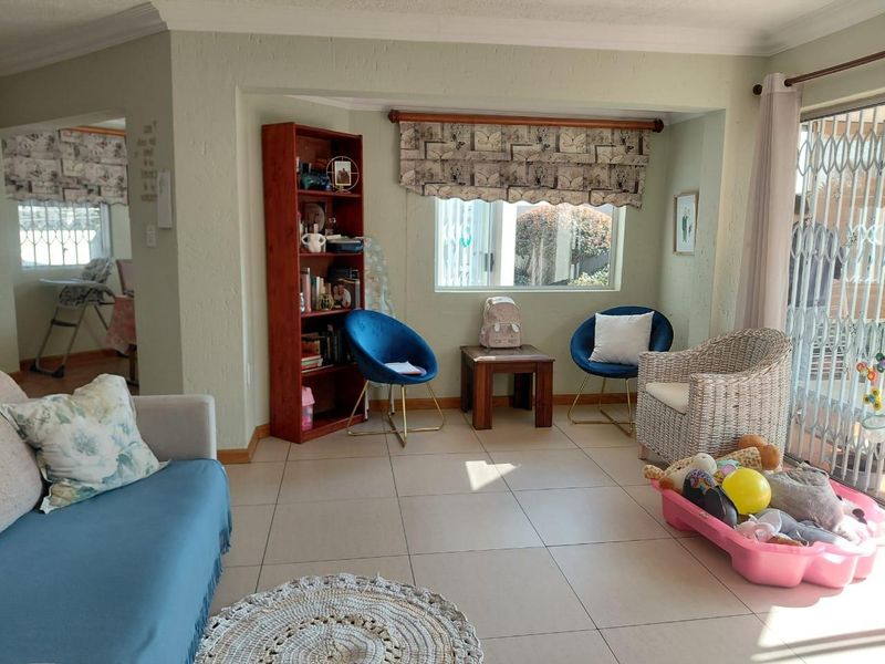 A bright living area featuring neutral tiled flooring, decorative cornicing, and a security gate leading to the exterior.
