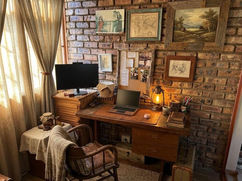 A cozy home office space featuring a rustic exposed brick wall and natural light from a side window.