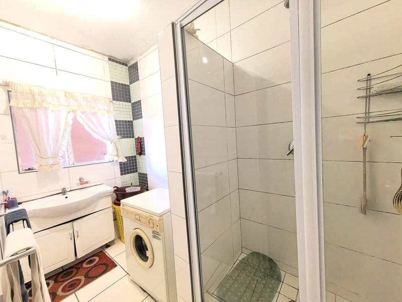 A functional bathroom featuring a shower enclosure, vanity cabinet with integrated basin, and tiled finishes, showing signs of wear and ceiling water damage.