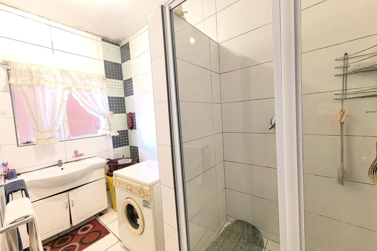 A functional bathroom featuring a shower enclosure, vanity cabinet with integrated basin, and tiled finishes, showing signs of wear and ceiling water damage.