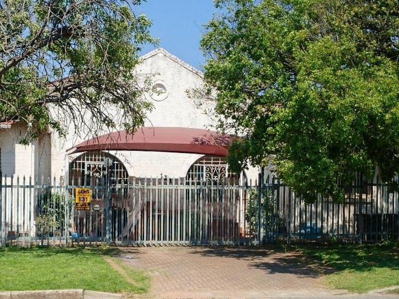 Front elevation of a residential property featuring a paved driveway, secure metal fencing, and an arched entrance canopy.