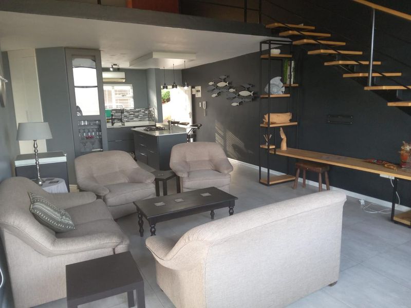 An open-plan living area featuring a modern kitchen with an island, tiled flooring, and a staircase leading to a mezzanine level.
